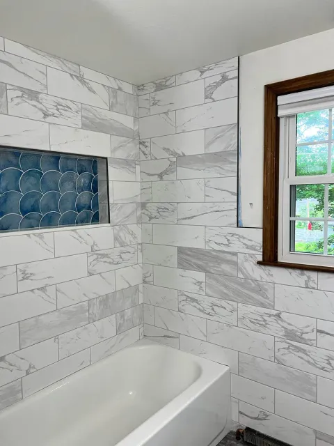 A bathroom with marble tiles , a tub and a window.