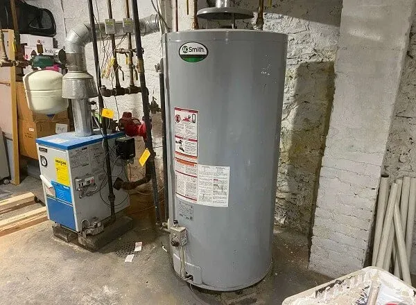 A water heater tank in a basement with plumbing and electrical connections.