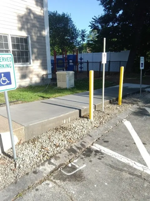 Accessible parking area with blue handicap sign, yellow bollards, and a paved walkway beside a building