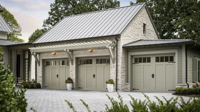 A three-car garage with light-colored brick, a metal roof, and light green garage doors on a cobblestone driveway.