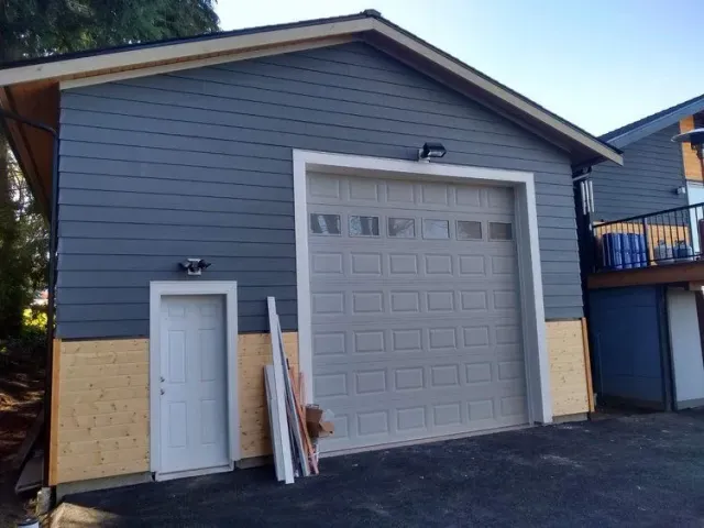 A  garage with large white door, white side entry door, and two tone look featured fresh blue siding and yellow foundation