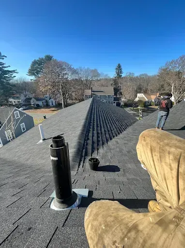 A person is standing on top of a roof with a chimney on it.