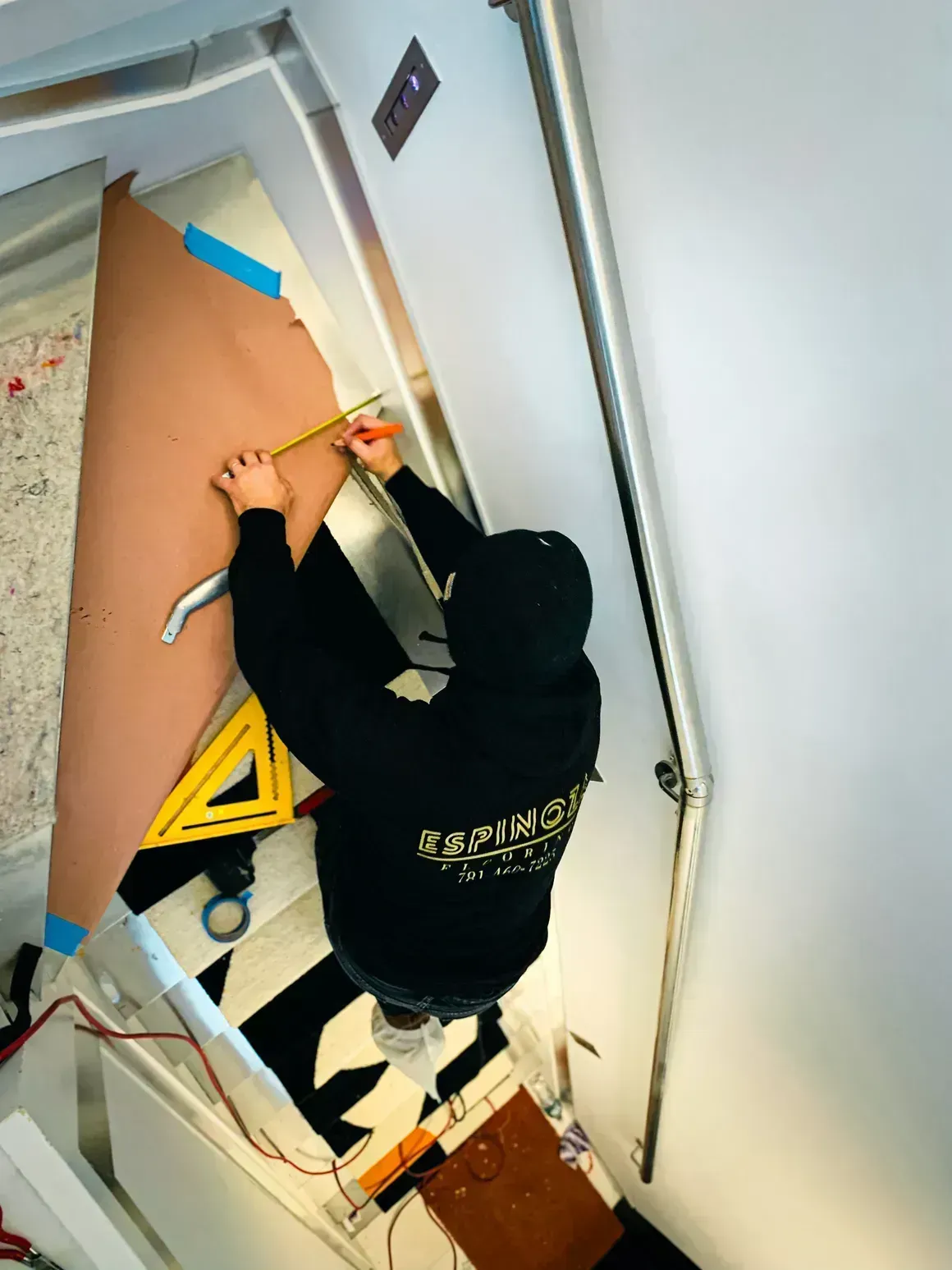Person measuring a large brown material on stairs, using a ruler and triangle.