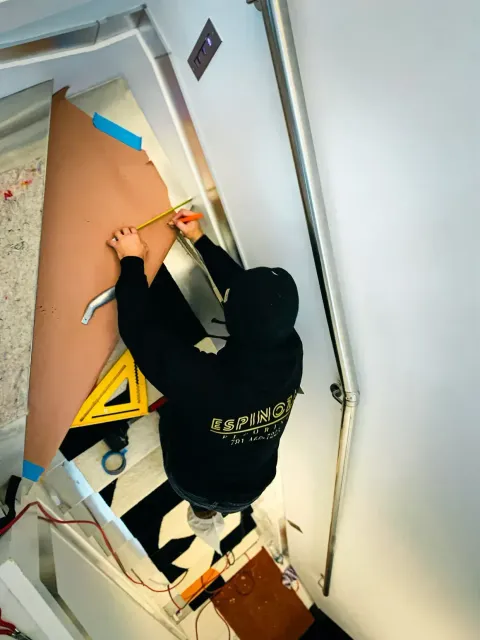 Person measuring a large brown material on stairs, using a ruler and triangle.