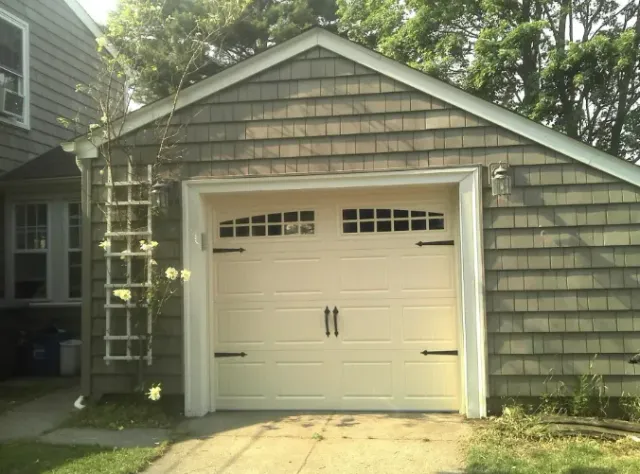 Tan garage door with black hardware, surrounded by weathered brown siding.
