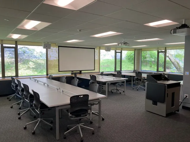 A large room with tables and chairs and a projector screen.