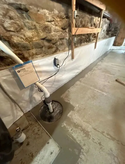 Plumbing pipe assembly on a basement floor beside a stone wall