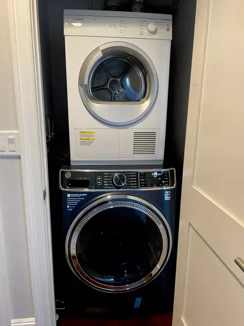 Stacked white dryer and black washer in a narrow laundry closet.