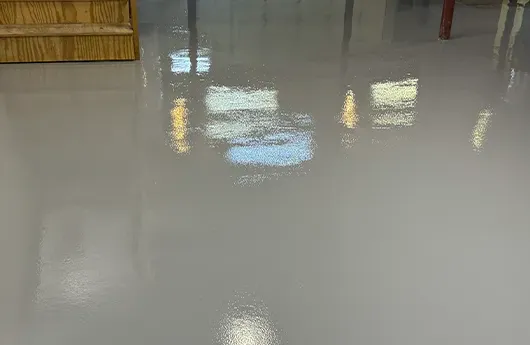 Industrial-grade high-gloss solid color epoxy flooring reflecting overhead lights in a clean commercial workspace.
