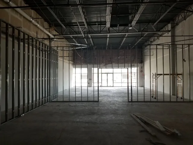 Interior of a building under construction with metal framing, exposed ceiling, and large front windows.