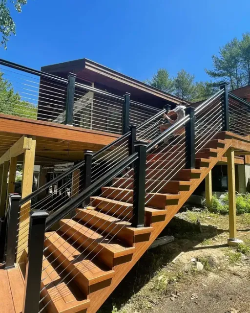 Wooden outdoor staircase with black railings leading to a raised deck under a blue sky