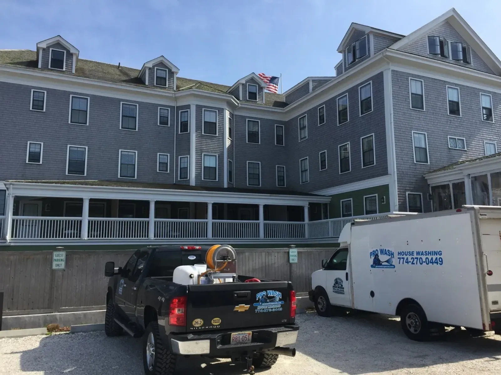 A multi-story grey building with a white porch; a black pickup truck and white van are parked in front.