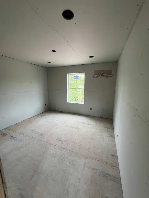 Empty room with unfinished drywall and concrete floor, single window, recessed lighting.