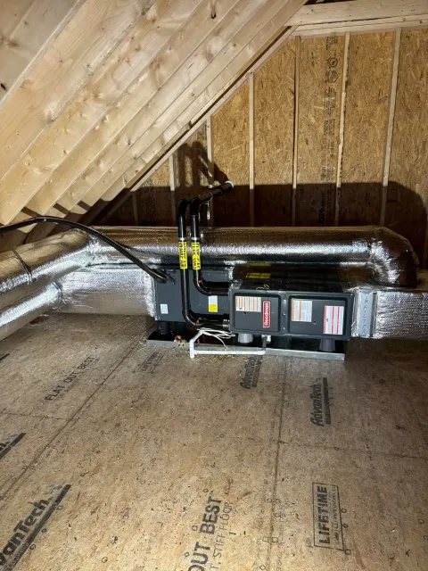 Attic HVAC unit with insulated ducts under a sloped wooden roof framing.