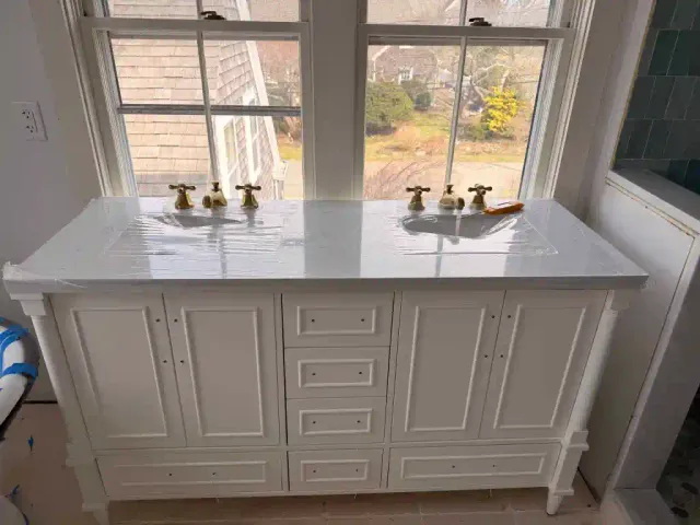 Elegant bathroom vanity with two sinks and gold fixtures near large window.