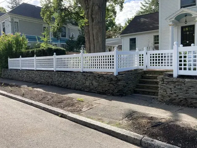 White picket fence and stacked stone wall along a blue house on a quiet residential street.