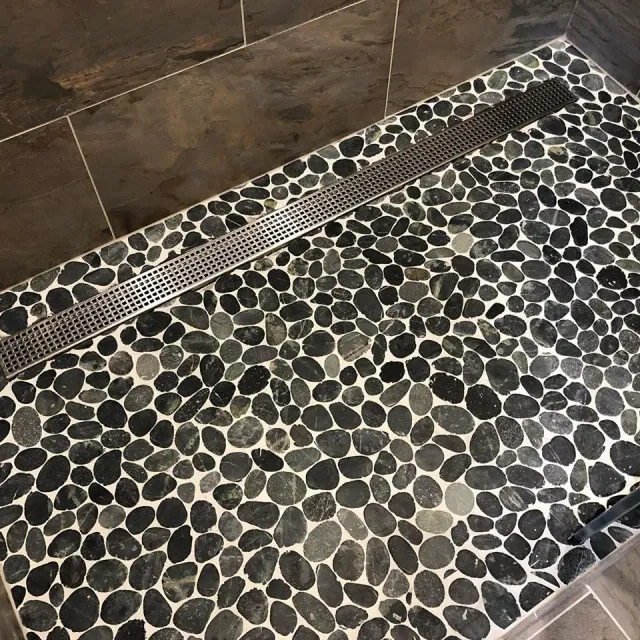 A shower stall with a black and white tile floor and a drain.