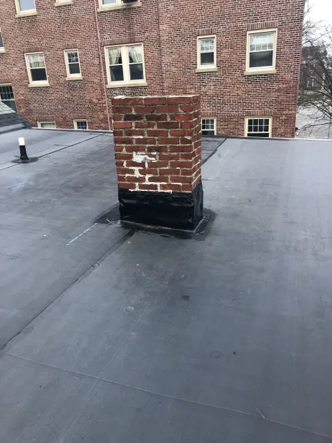 Flat black rooftop with a brick chimney and red brick building wall in the background