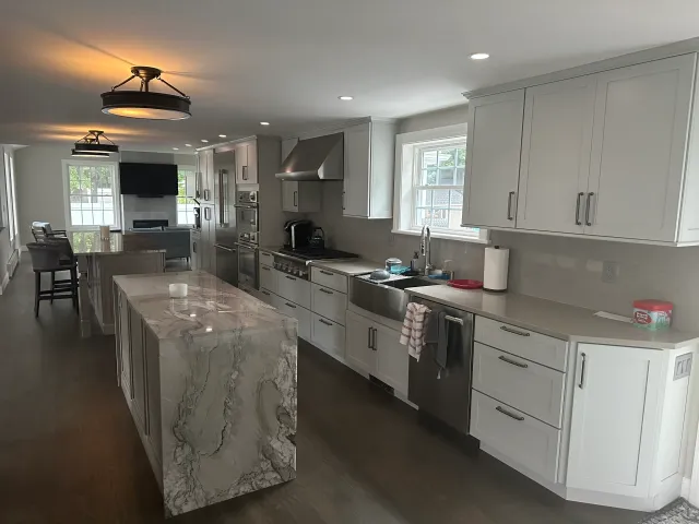 Modern kitchen in Boston featuring white cabinets, a marble island, stainless steel appliances, and large windows for natural light.