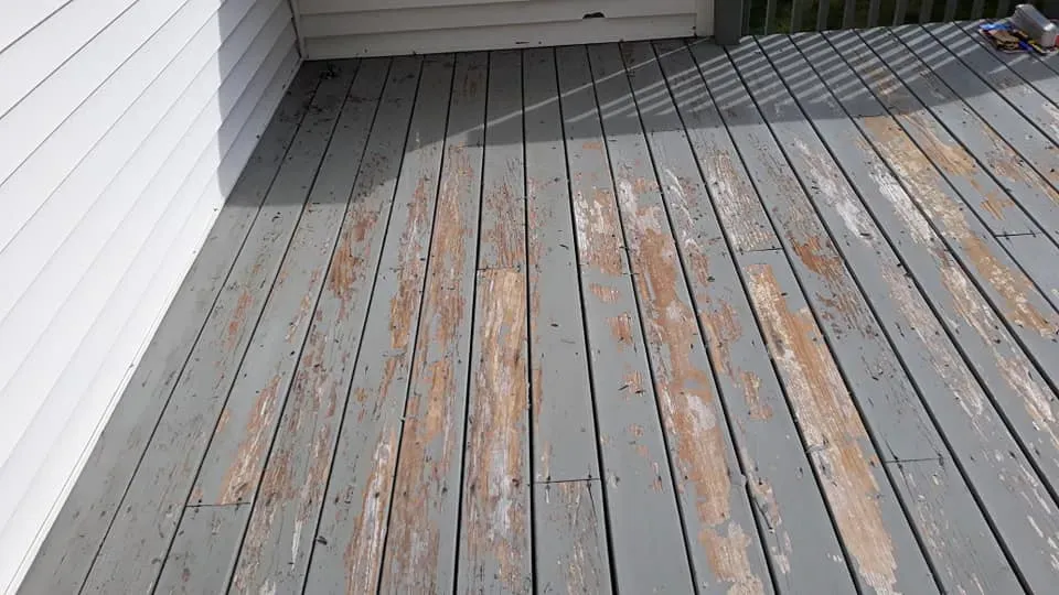 A wooden deck with peeling paint and a white house in the background.