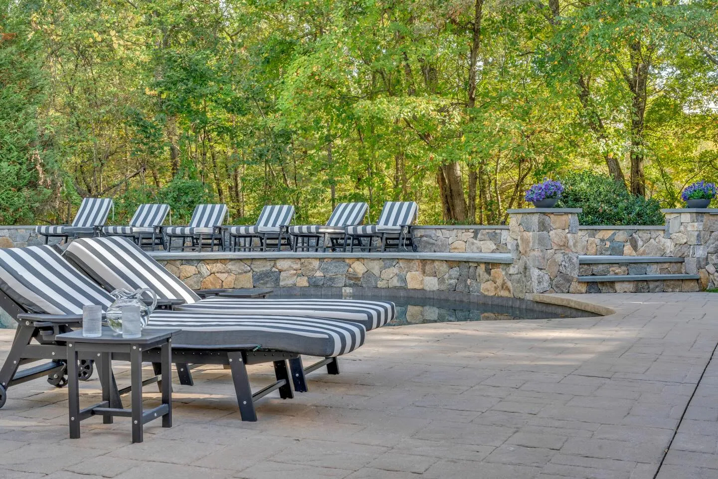 Custom pool deck with natural stone retaining wall and lounge seating built by Precision Excavation in Foxborough, MA
