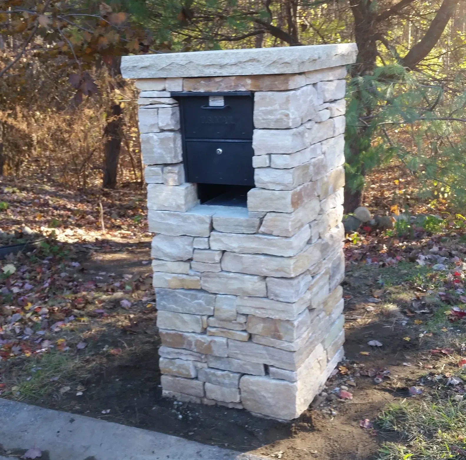 Stone mailbox pillar with black mailbox.