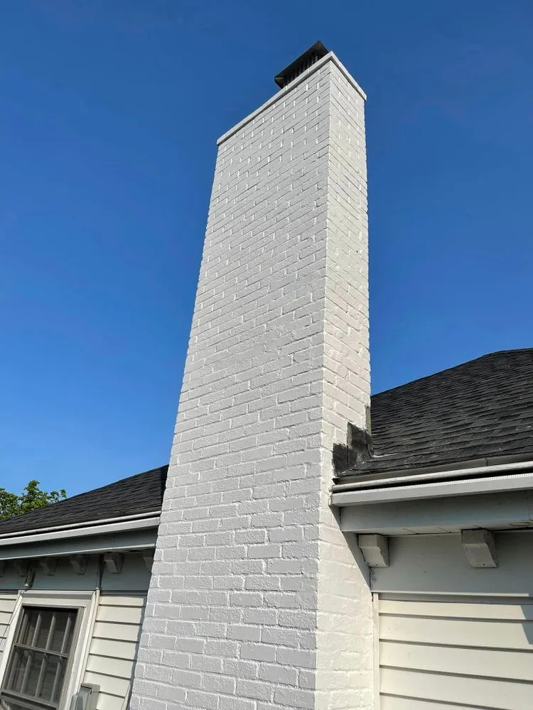 Tall masonry chimney refinished in a light coating against a clear blue sky