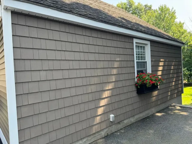 Side view of a gray house with white trim, a window box of red flowers, and a driveway beside it
