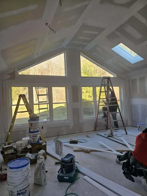 Before: vaulted room with taped and mudded drywall, ladders and paint buckets