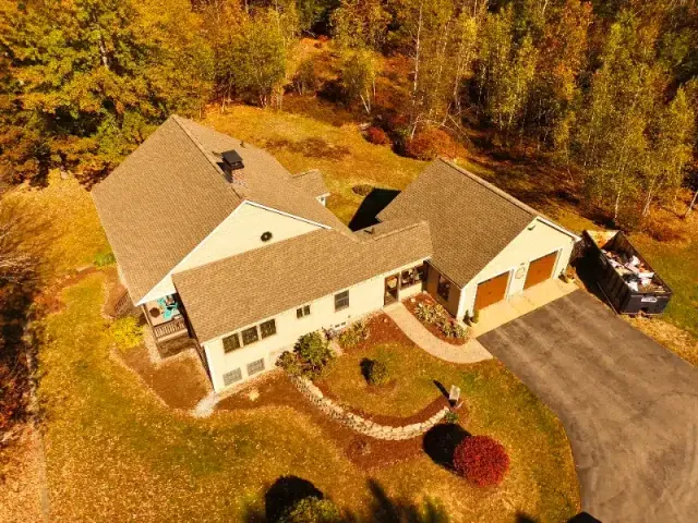 Aerial view of a spacious house with a landscaped yard, surrounded by trees in autumn colors, and a driveway leading to a garage.