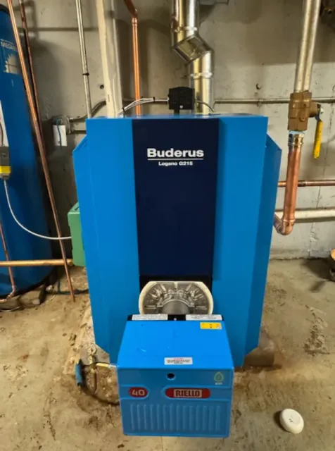 Blue Buderus boiler with attached blue control panel, copper pipes, in a basement setting.