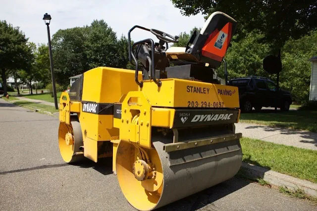 A yellow Dynapac asphalt roller sits on a residential street during the day.