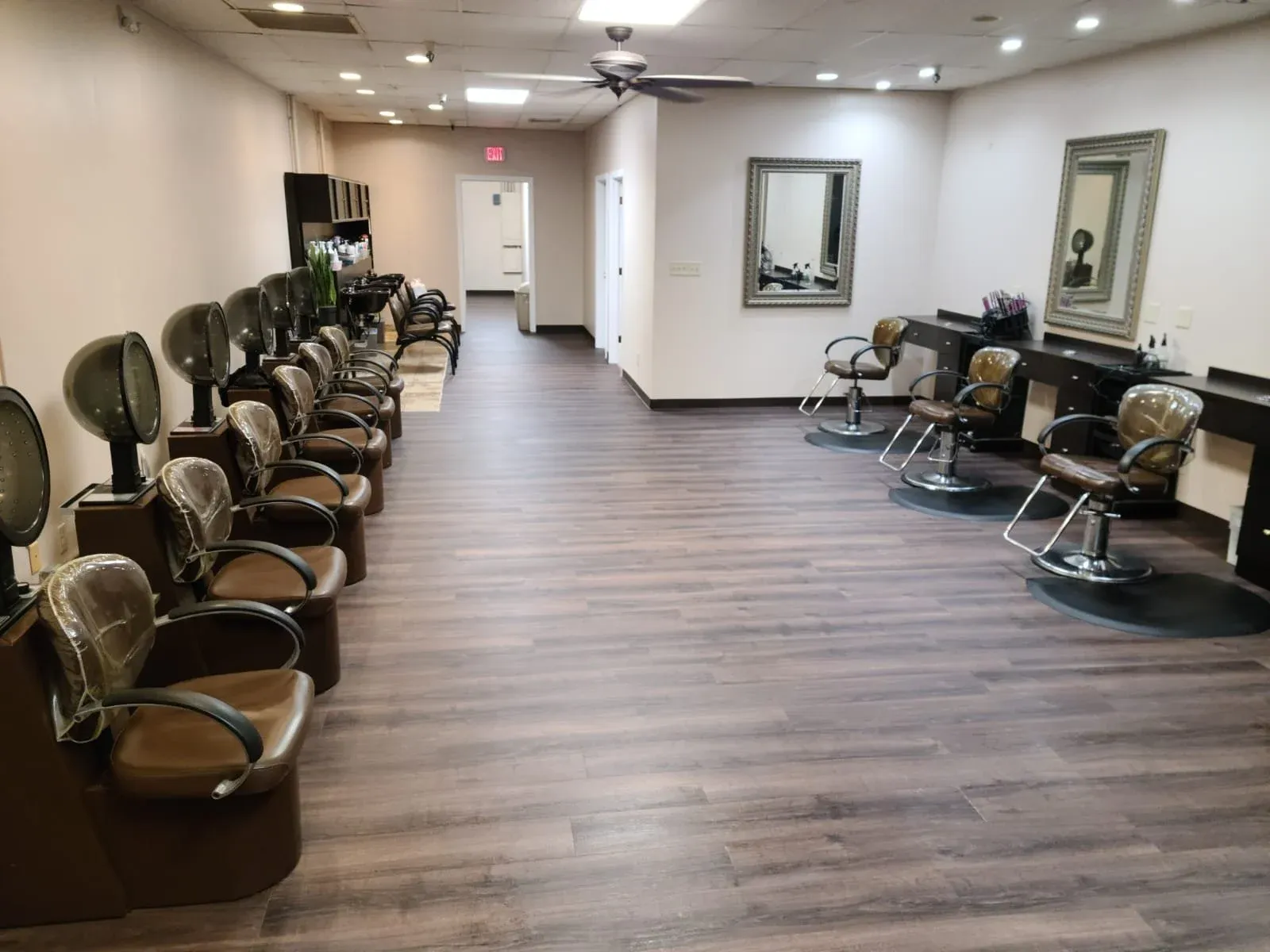 Empty hair salon with hair washing stations on the left, styling chairs and mirrors on the right, and wooden flooring.