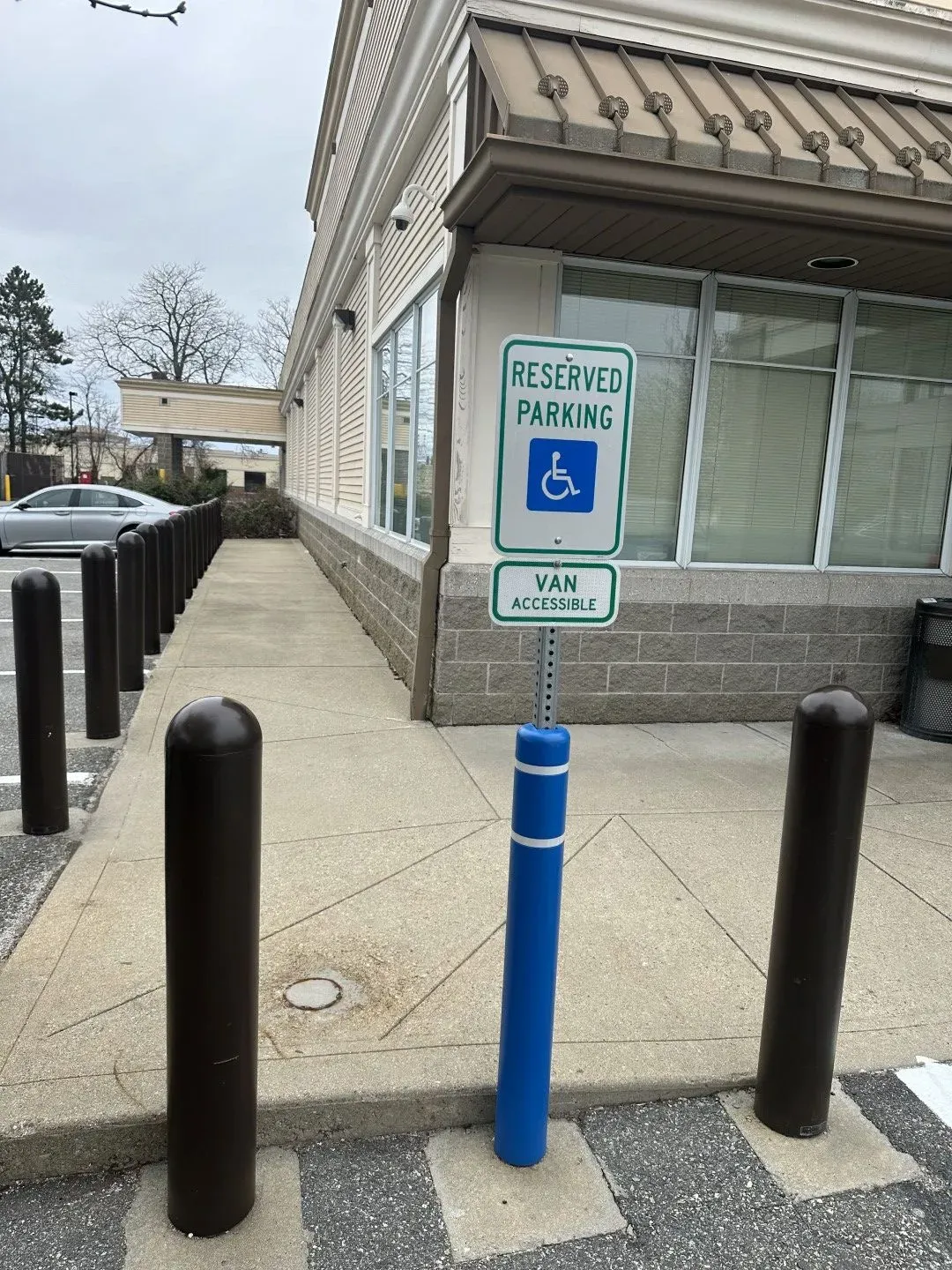 Handicap parking sign beside a storefront walkway with bollards and a blue post