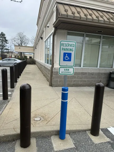 Handicap parking sign beside a storefront walkway with bollards and a blue post