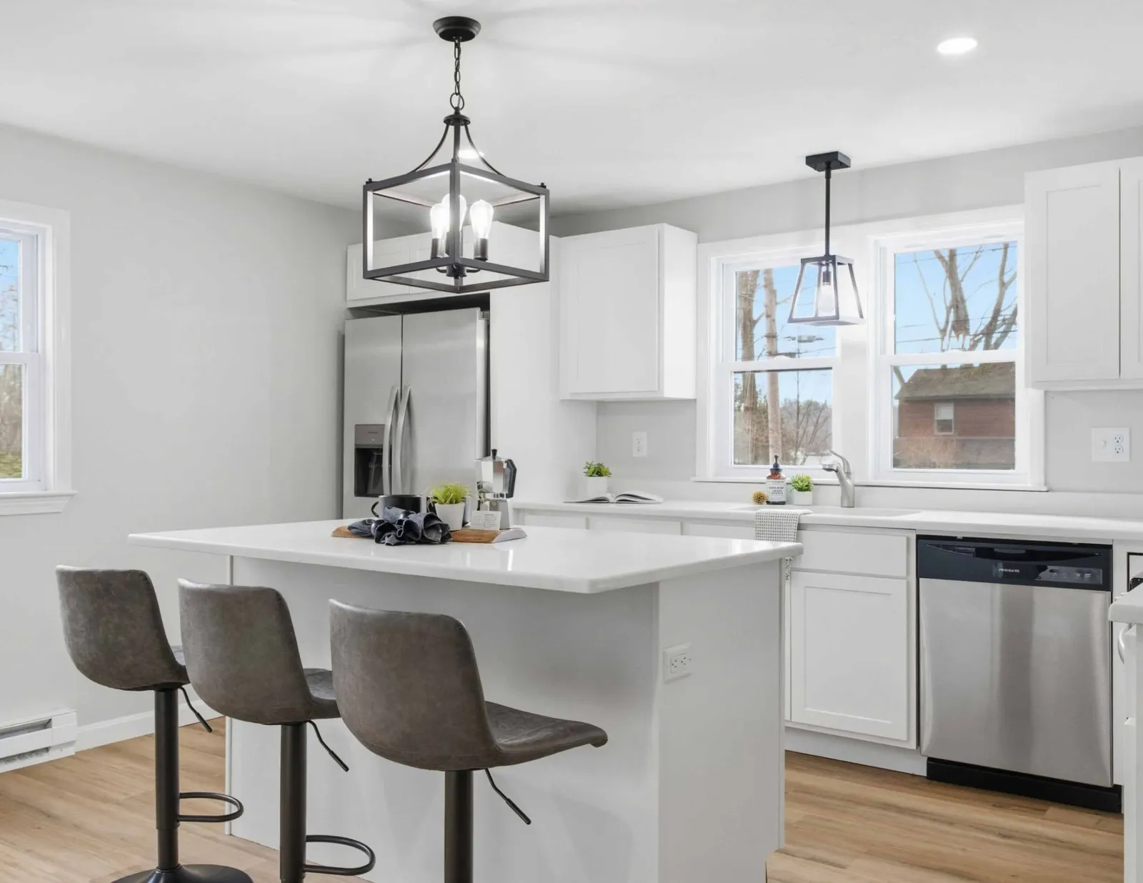 Modern kitchen with white cabinets, island with three gray stools, stainless steel fridge and dishwasher.