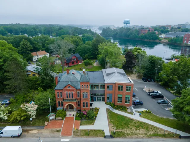 Aerial view of a historic brick building by a serene river in Maine.