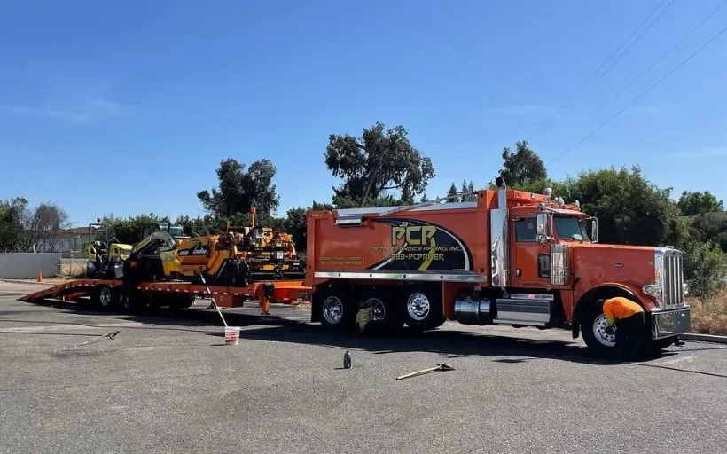 Orange tow truck hauling equipment in a parking lot on a sunny day
