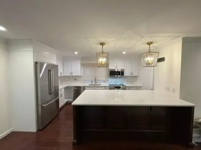 Modern kitchen with white cabinets, stainless steel appliances, dark wood island, and gold light fixtures.