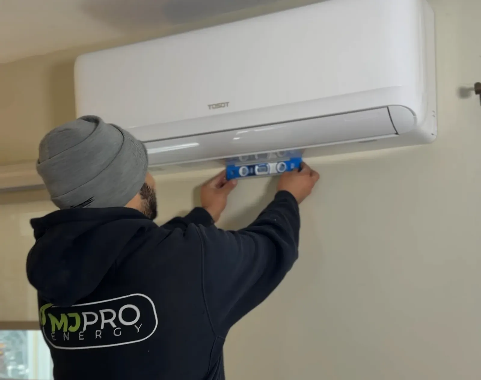 MJ Pro Energy technician leveling a Tosot mini split head on a wall