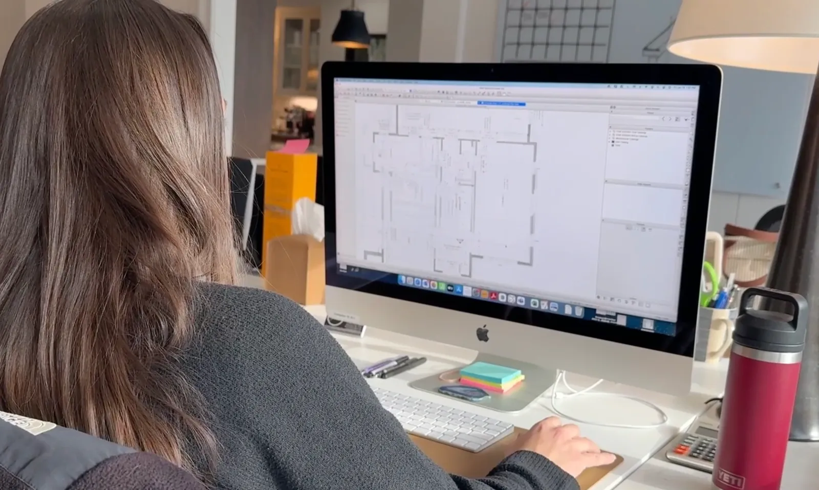 A brunette woman uses a desktop computer to look at floor plans