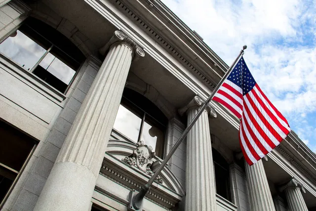 American flag hanging from a classical building with white fluted columns.