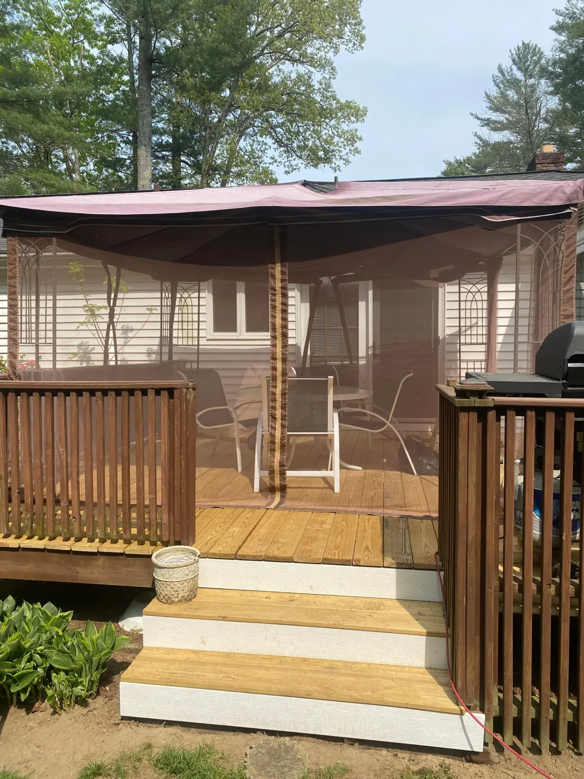 A wooden deck with white steps, a screened-in gazebo area, patio furniture, and a house in the background.