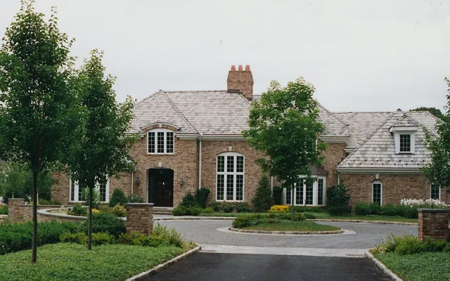 A large brick house with a slate roof, surrounded by trees and a landscaped yard with a curved driveway.