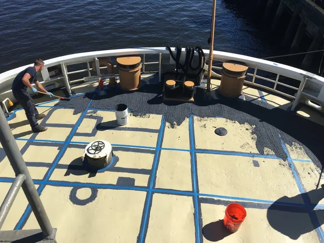 Applicator rolling a specialty coating onto a marine deck over taped panel joints