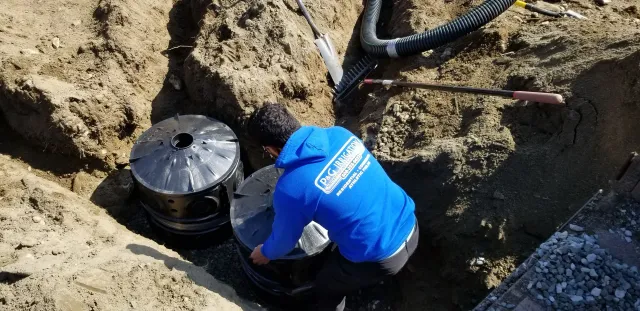 A man in a blue hoodie is working on a septic tank in the dirt.
