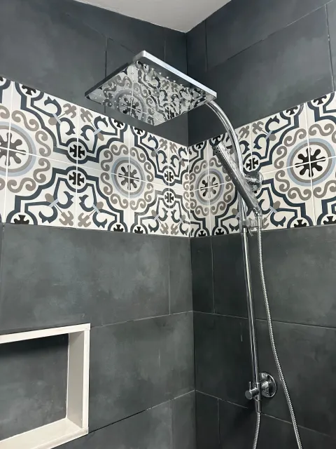 A modern shower with dark gray tiles, a decorative patterned tile strip, a rain showerhead, and a handheld showerhead.