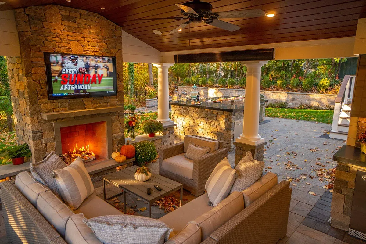 Covered outdoor living room with stone fireplace, TV, and bar area designed by Land Design Associates in Needham, Massachusetts.