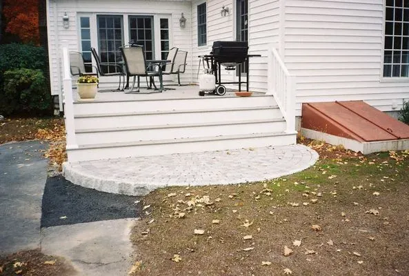 White home exterior with steps leading to a patio area. A circular stone area at the base of the steps.