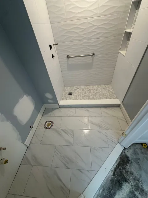 Small bathroom with white tile floor, shower stall, and gray-blue walls.